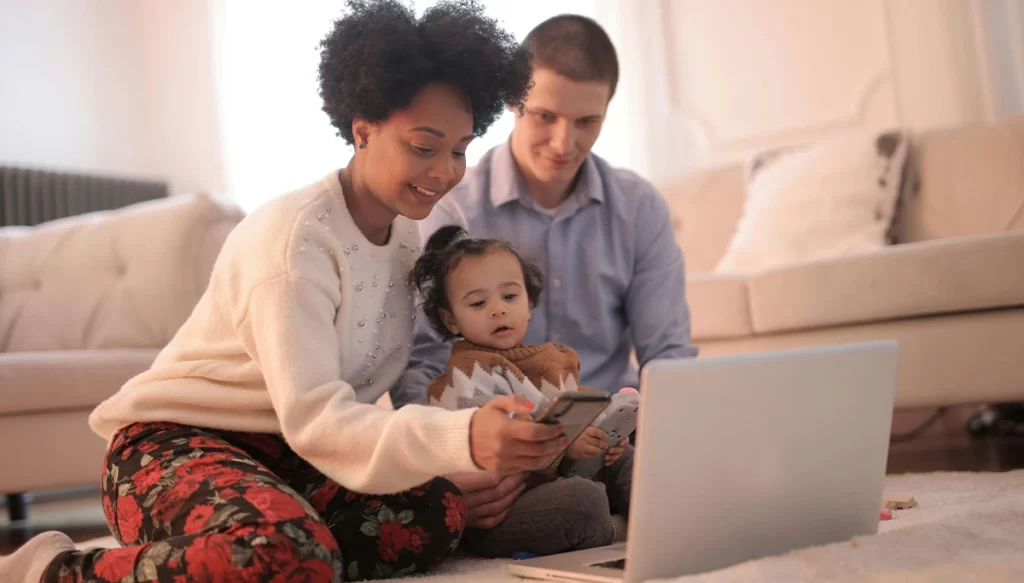 mother father and young girl sitting on the living room floor infront of a laptop