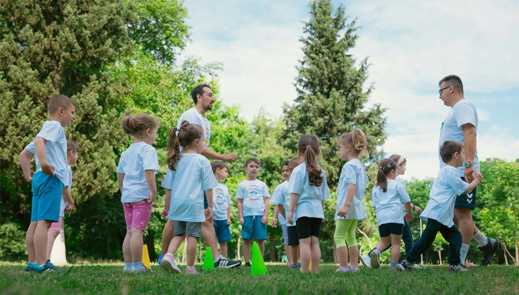 Group of children and teachers playing and learning in a sunny park setting.