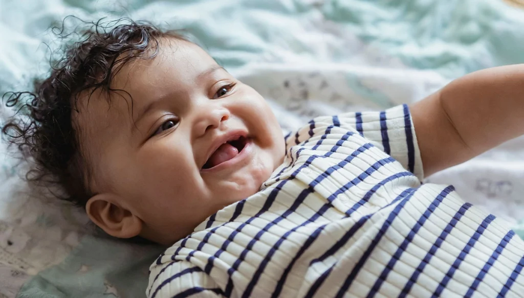 baby lying on a blanket smiling happily in a striped onesie
